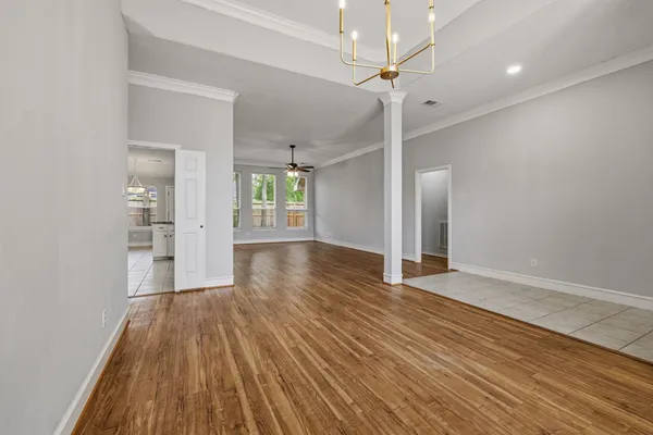 an empty room with wooden floor chandelier fan and windows