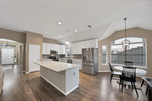 a kitchen with stainless steel appliances a refrigerator a stove a sink a dining table and chairs with wooden floor