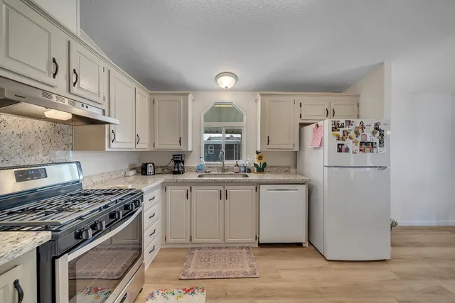 a kitchen with stainless steel appliances granite countertop a stove a sink dishwasher and refrigerator with wooden floor