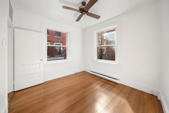 an empty room with wooden floor chandelier fan and windows