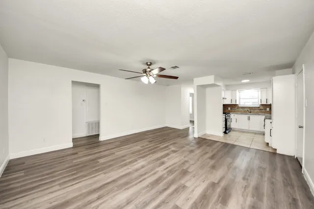 a view of an empty room with wooden floor and a kitchen