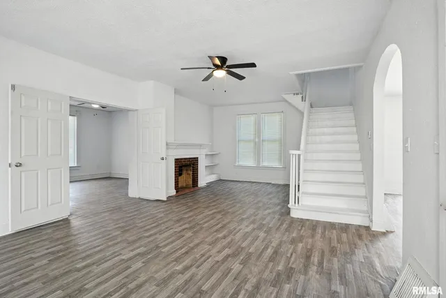 an empty room with wooden floor fireplace and windows