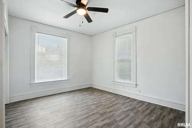 an empty room with wooden floor fan and windows