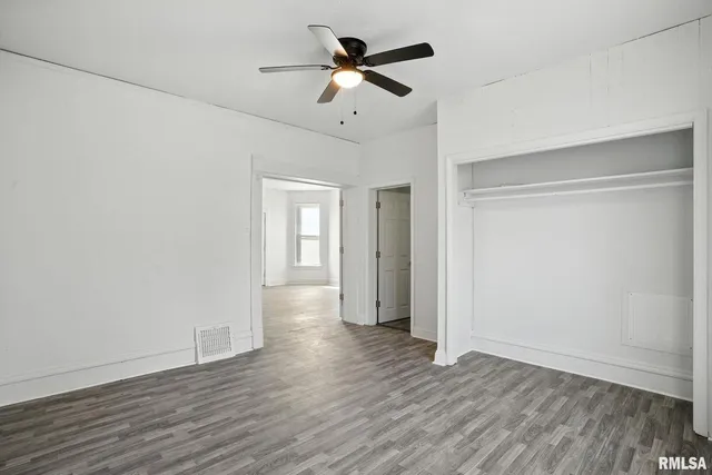 a view of an empty room with wooden floor and a ceiling fan