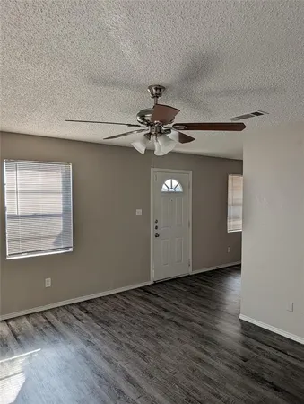 an empty room with wooden floor chandelier fan and windows