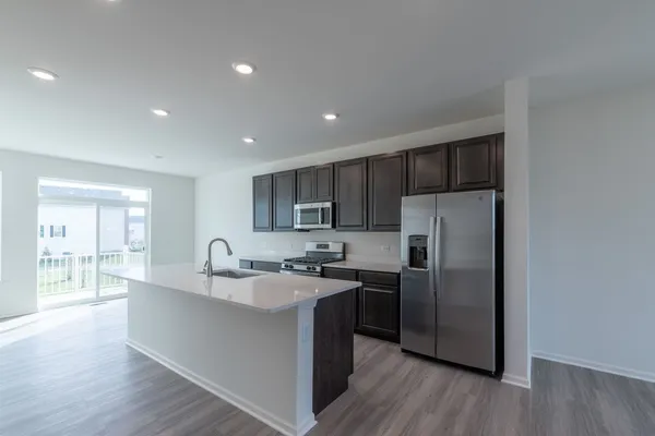 a kitchen with stainless steel appliances granite countertop a stove a refrigerator a sink a dining table and chairs with wooden floor