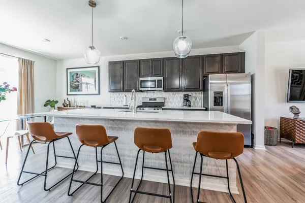 a kitchen with stainless steel appliances granite countertop a stove top oven a refrigerator a sink and chairs