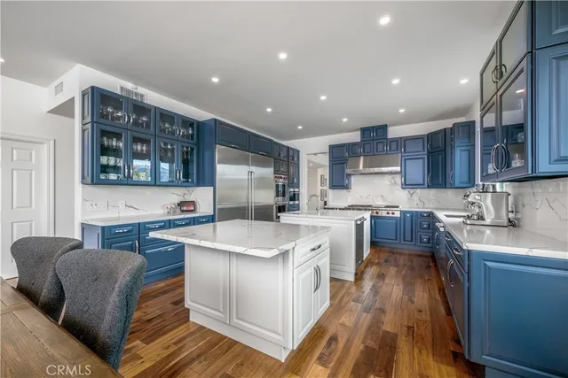 a kitchen with stainless steel appliances granite countertop a stove top oven a sink dishwasher and a refrigerator with wooden floor