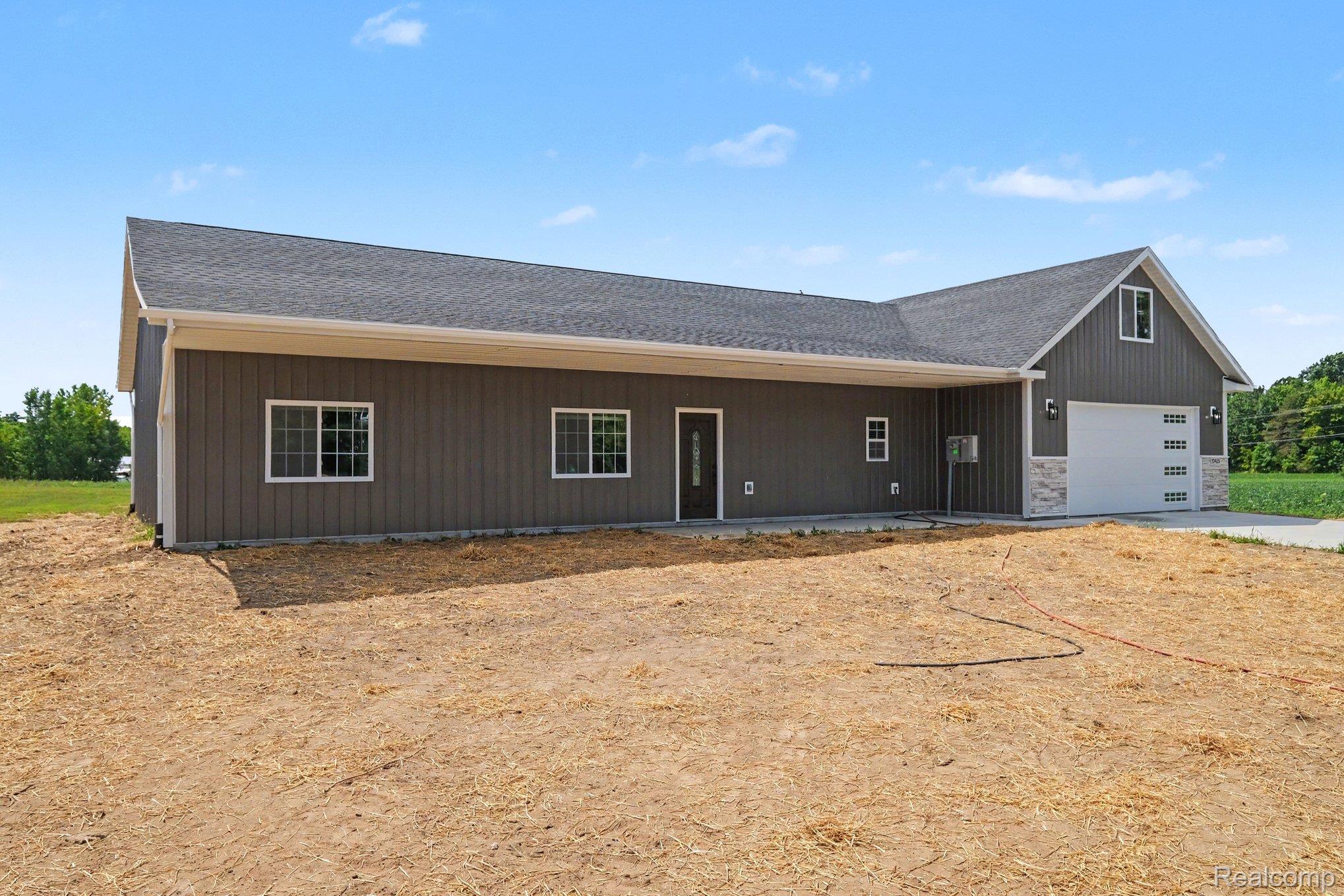 12425 Miller Road Lennon, MI 48449 - Photo 4 of 26 Modern farmhouse-style exterior featuring vertical siding in a deep gray finish and a contrasting white garage door