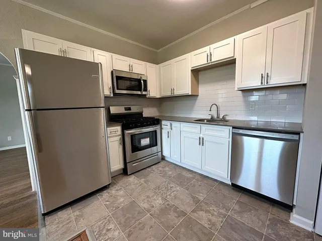 a kitchen with stainless steel appliances granite countertop white cabinets a refrigerator a sink a stove a microwave and wooden cabinets