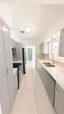 a large white kitchen with a sink and dishwasher a stove top oven with wooden floor