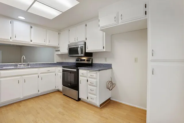 a kitchen with stainless steel appliances granite countertop white cabinets a sink a stove a microwave and a refrigerator