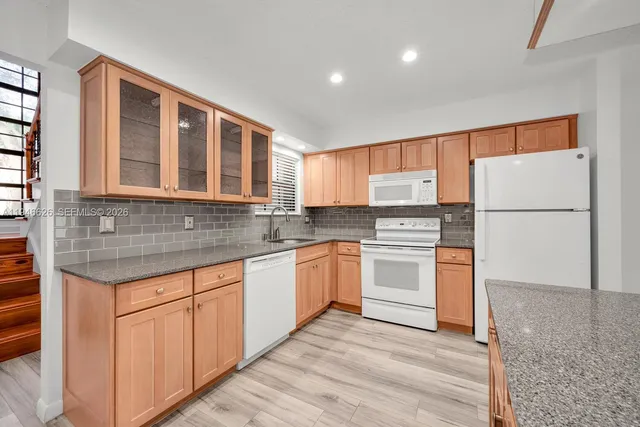 a kitchen with granite countertop stainless steel appliances a refrigerator cabinets and wooden floor