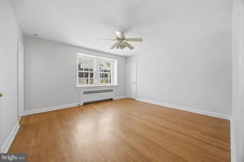 an empty room with wooden floor ceiling fan and windows