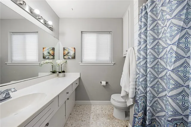 a bathroom with a granite countertop toilet a sink a mirror a window and a shower