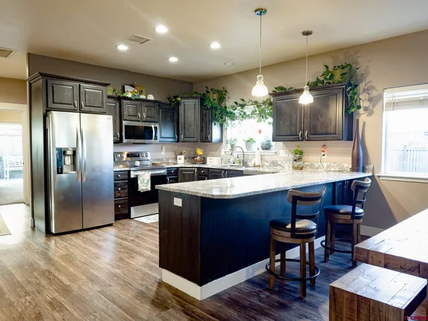 a kitchen with stainless steel appliances granite countertop a refrigerator a sink dishwasher a stove and a dining table with wooden floor