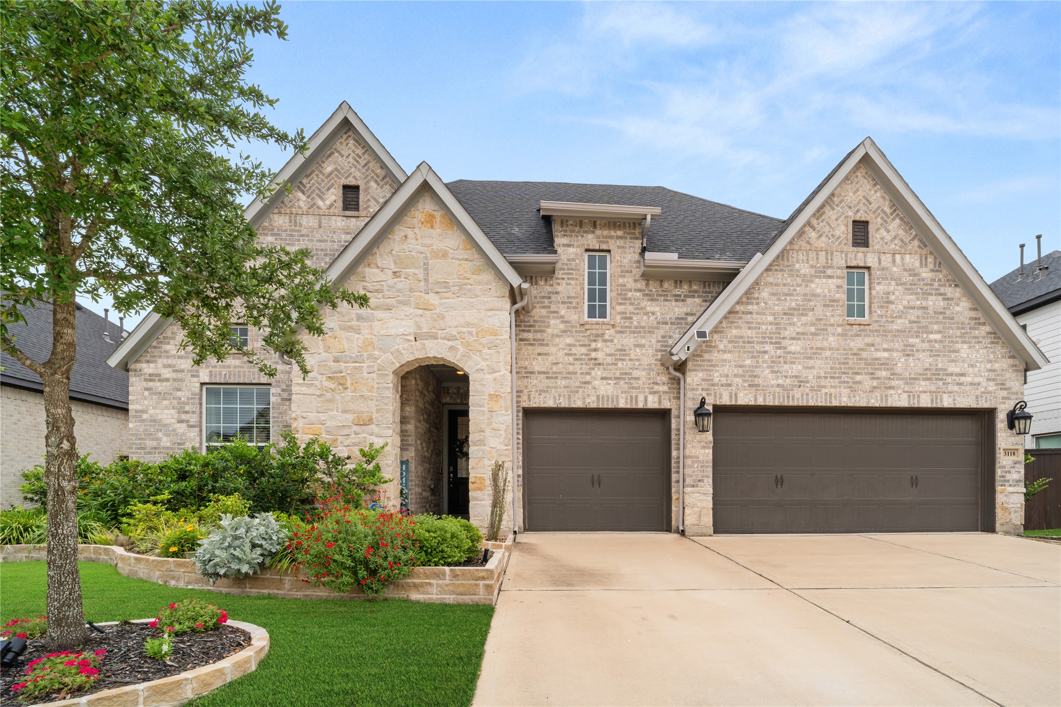 Front Exterior – Attractive brick and stone exterior with mature landscaping and a spacious driveway leading to a three-car garage.