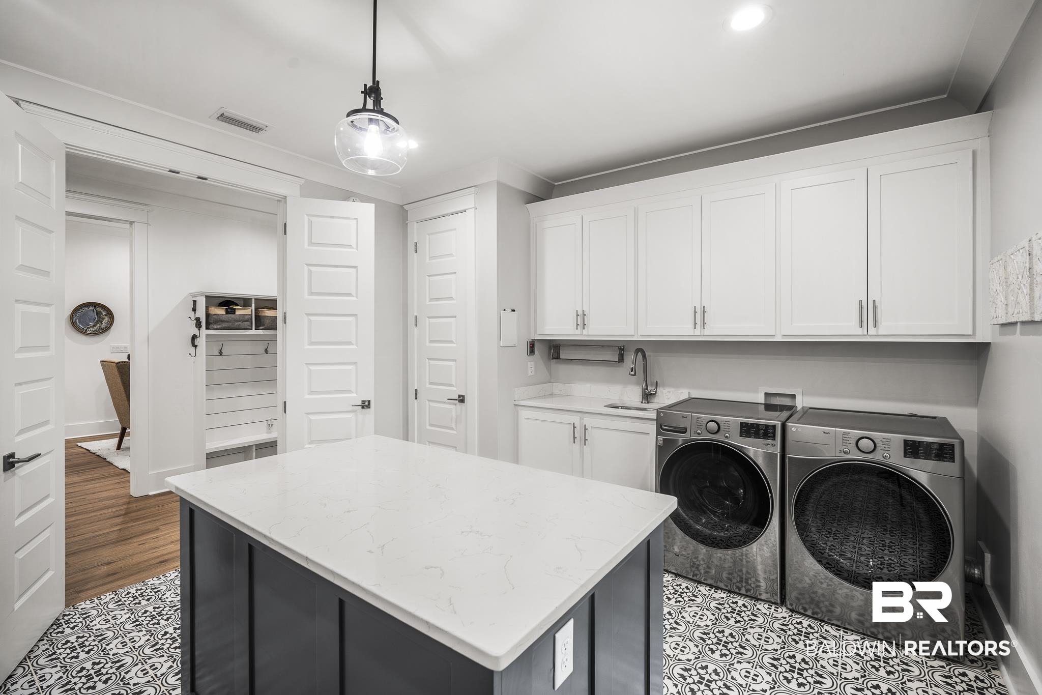 21702 Pillars Street Fairhope, AL 36532 - Photo 17 of 54 Laundry room featuring patterned tile flooring, a central island with a light-toned countertop, white cabinetry with silver hardware, and a utility sink