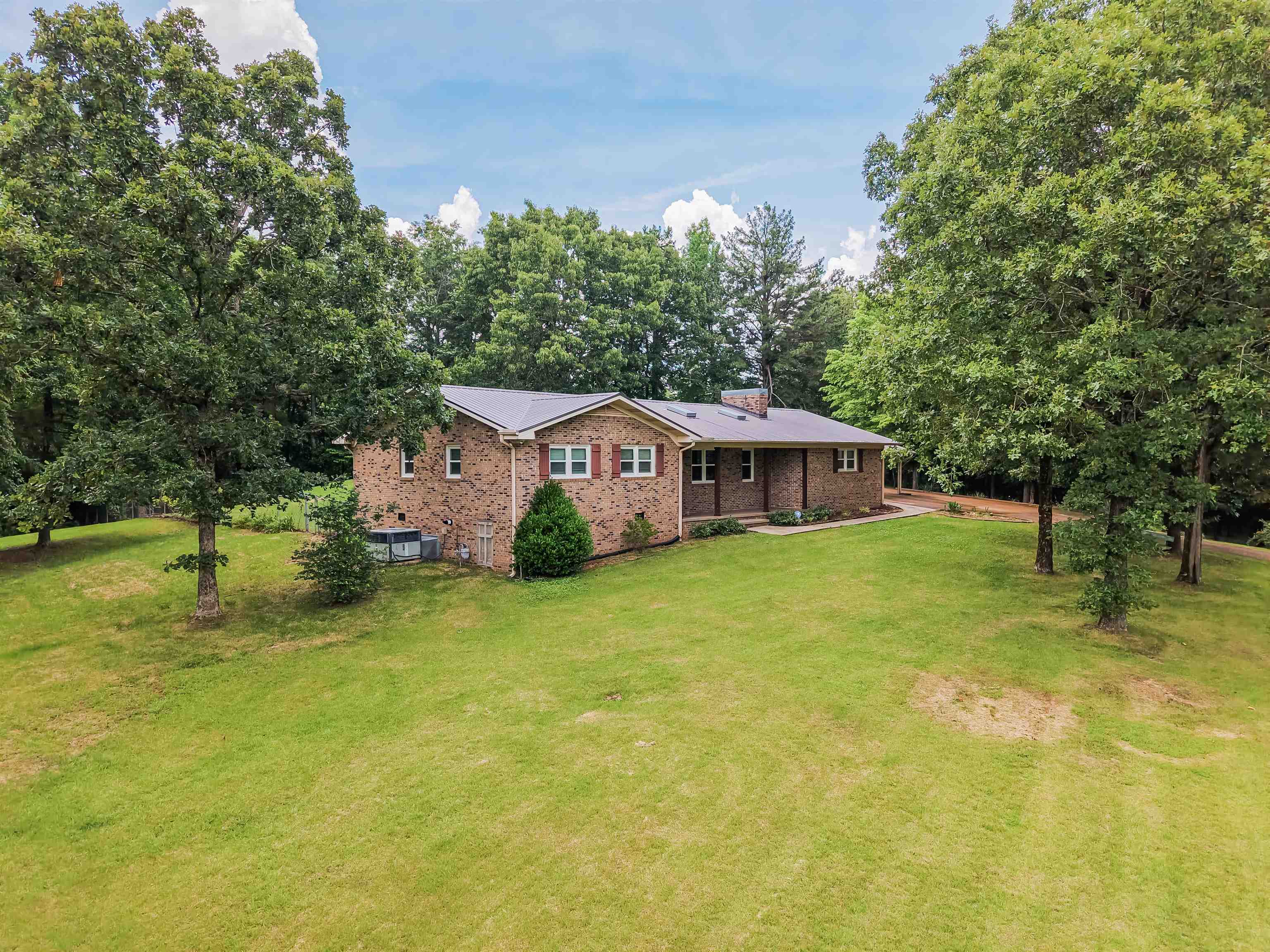 Brick ranch-style residence featuring a metal roof and an expansive lawn
