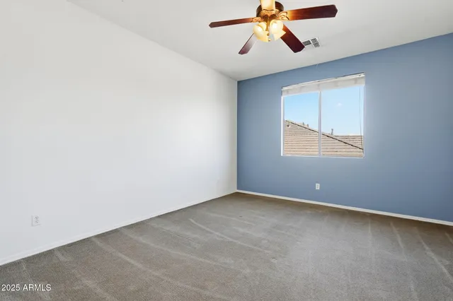 an empty room with chandelier fan and windows