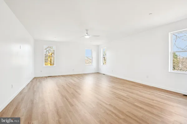 a view of an empty room with wooden floor and a ceiling fan