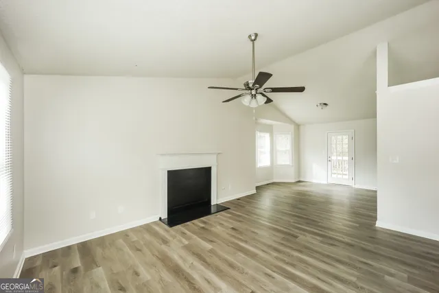 an empty room with wooden floor fireplace and windows