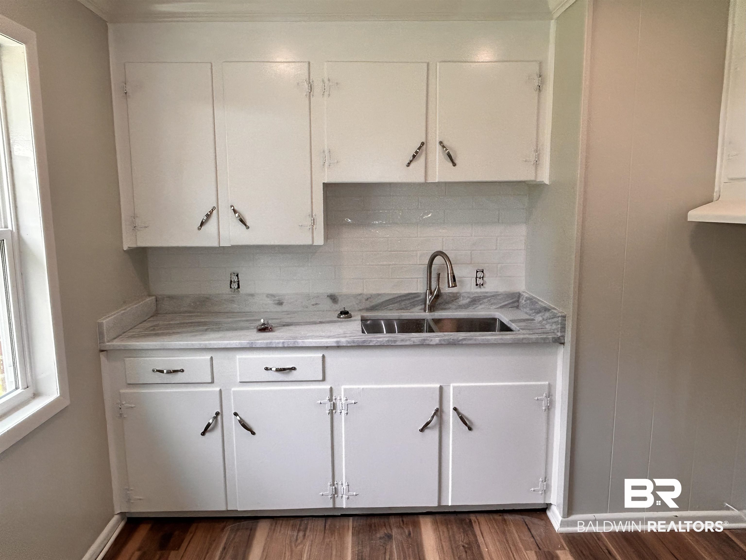 7870 Bradley Road Brewton, AL 36426 - Photo 4 of 8 Kitchenette featuring white cabinetry, a dual-basin stainless steel sink with a gooseneck faucet, light-toned backsplash, and wood-finish flooring