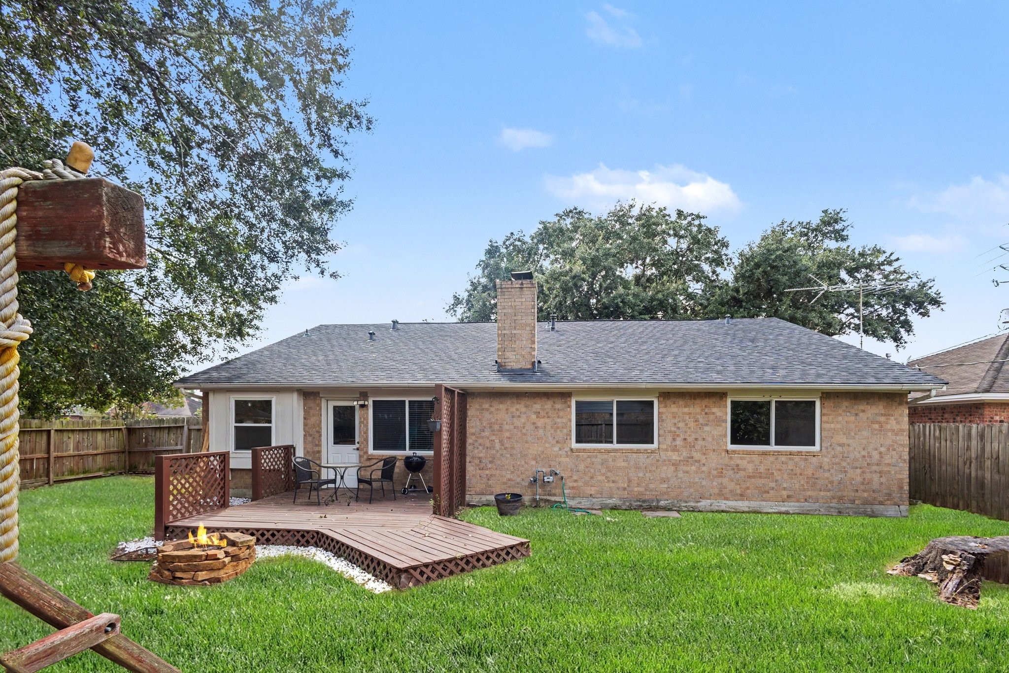 21902 Meadowhill Drive Spring, TX 77389 - Photo 20 of 28 Charming backyard with a spacious wooden deck, perfect for outdoor dining and relaxation, complemented by a cozy fire pit and lush green lawn, all enclosed by a wooden fence for privacy.