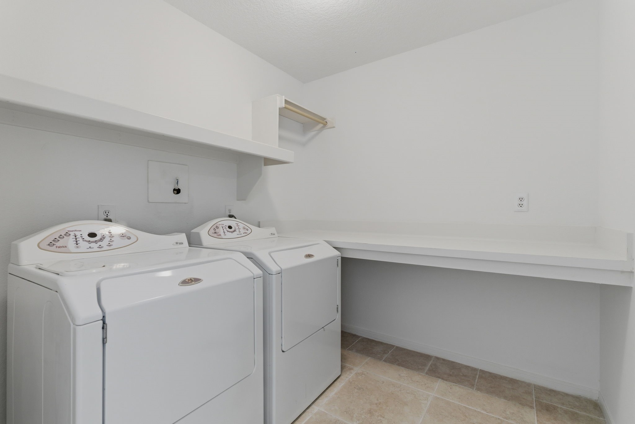 11 Dovewing Place Spring, TX 77382 - Photo 24 of 32 This photo shows a spacious laundry room with a washer and dryer, white walls, tiled flooring, and a long countertop for folding clothes. There is also a shelf for additional storage.