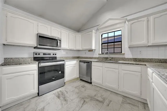 a kitchen with granite countertop white cabinets stainless steel appliances and a window