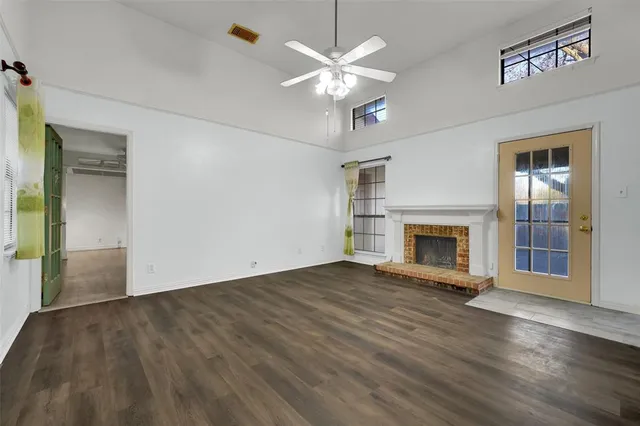 an empty room with wooden floor a chandelier fan a fireplace and windows