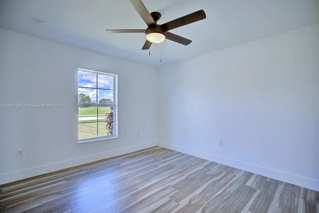 an empty room with wooden floor ceiling fan and windows