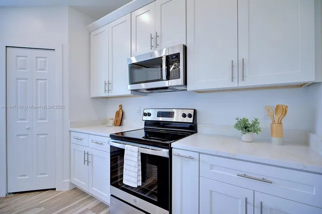 a kitchen with stainless steel appliances granite countertop white cabinets a stove a sink and a white wooden floor