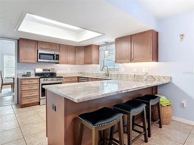 a kitchen with granite countertop a stove a sink dishwasher a refrigerator with wooden cabinets and chairs