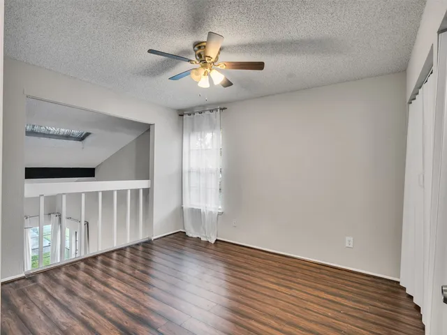 a view of an empty room with wooden floor and a ceiling fan
