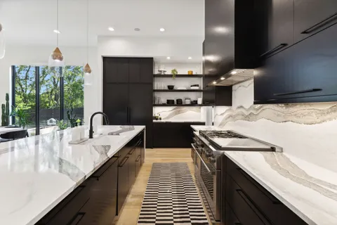 a large kitchen with stainless steel appliances kitchen island a large counter top a stove a chimney a sink and living room view