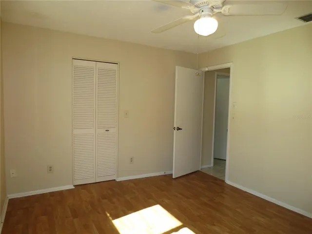a view of an empty room with wooden floor and fan
