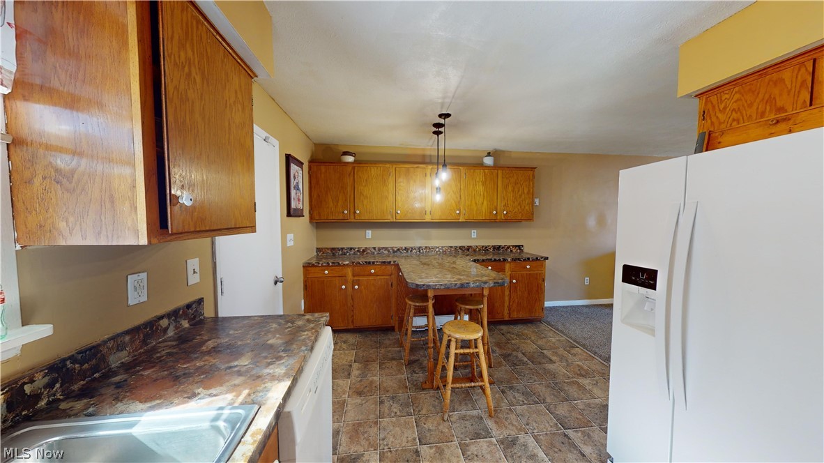 6970 Bushnell Road Conneaut, OH 44030 - Photo 18 of 28 Kitchen with white appliances, decorative light fixtures, dark tile floors, and a kitchen bar