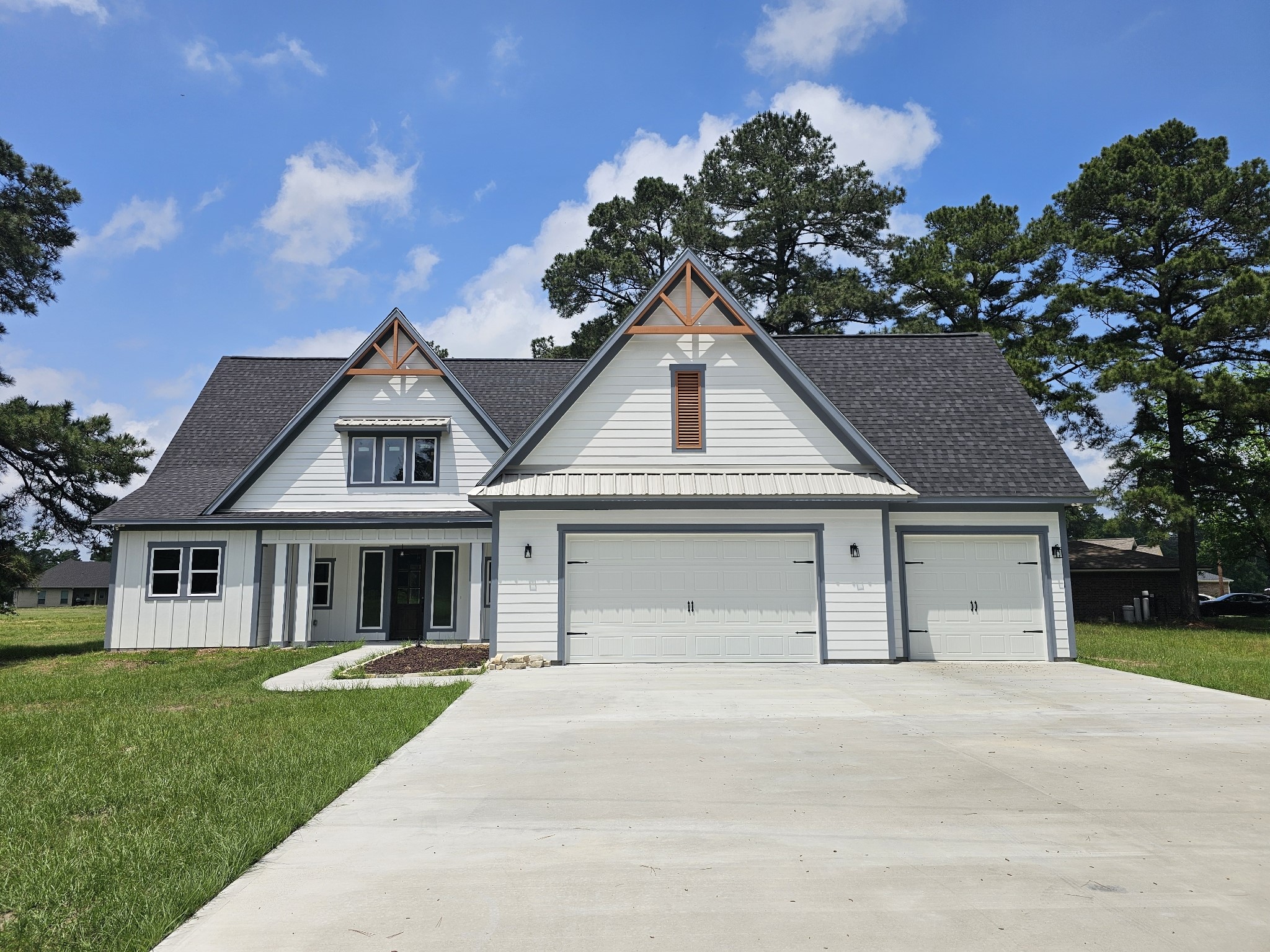 Modern farmhouse with a three-car garage, a charming gabled roof, and a large driveway.