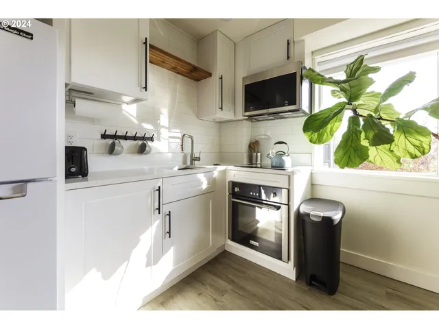 a kitchen with stainless steel appliances granite countertop a sink a stove a microwave a refrigerator with white cabinets and wooden floor