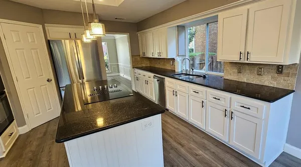 a kitchen with stainless steel appliances granite countertop a refrigerator a sink dishwasher a stove and white countertops with wooden floor