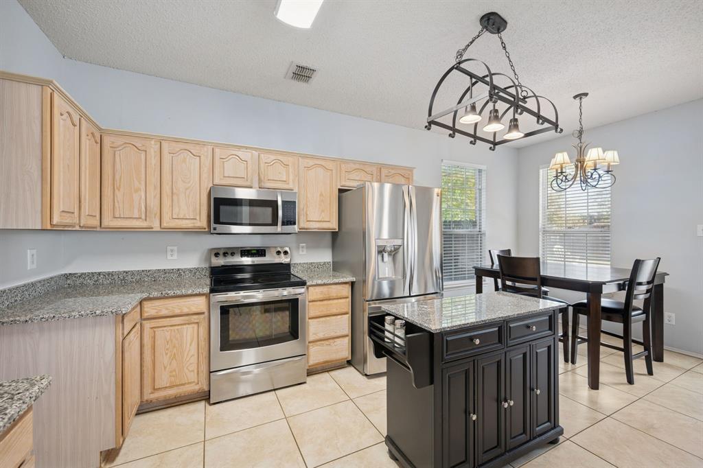 3304 Olympus Court Corinth, TX 76210 - Photo 16 of 40 a kitchen with stainless steel appliances granite countertop a stove a sink dishwasher a refrigerator and a dining table with the chandelier