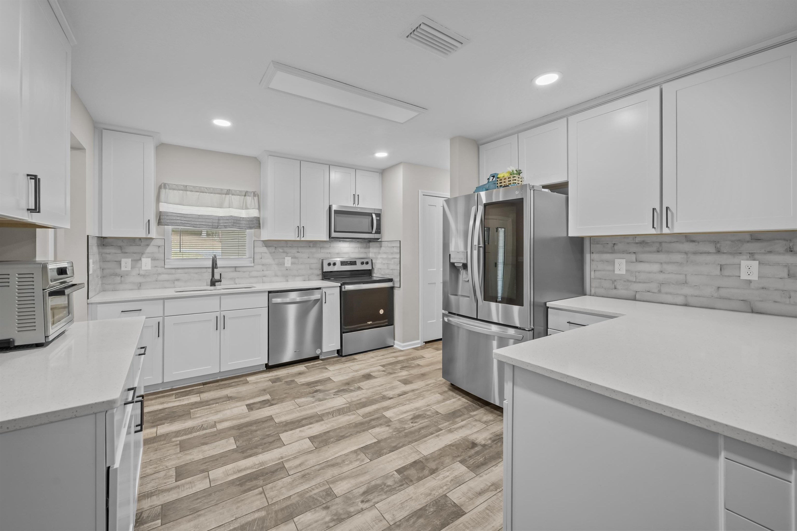 232 Kyte Road San Mateo, FL 32187 - Photo 11 of 36 Kitchen with white cabinets, appliances with stainless steel finishes, decorative backsplash, light wood finished floors, and recessed lighting