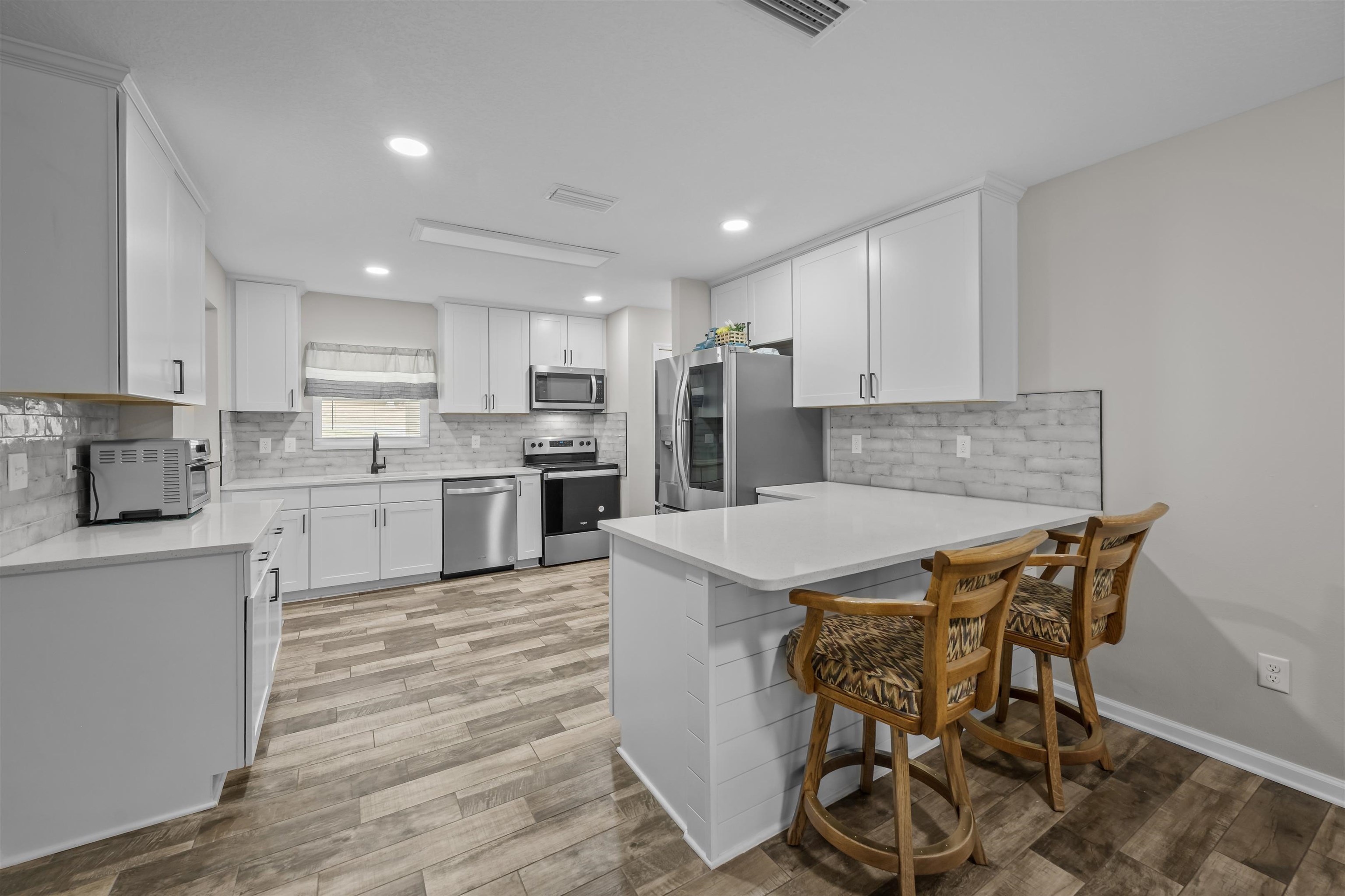 232 Kyte Road San Mateo, FL 32187 - Photo 9 of 36 Kitchen featuring white cabinetry, tasteful backsplash, stainless steel appliances, a peninsula, and light stone counters