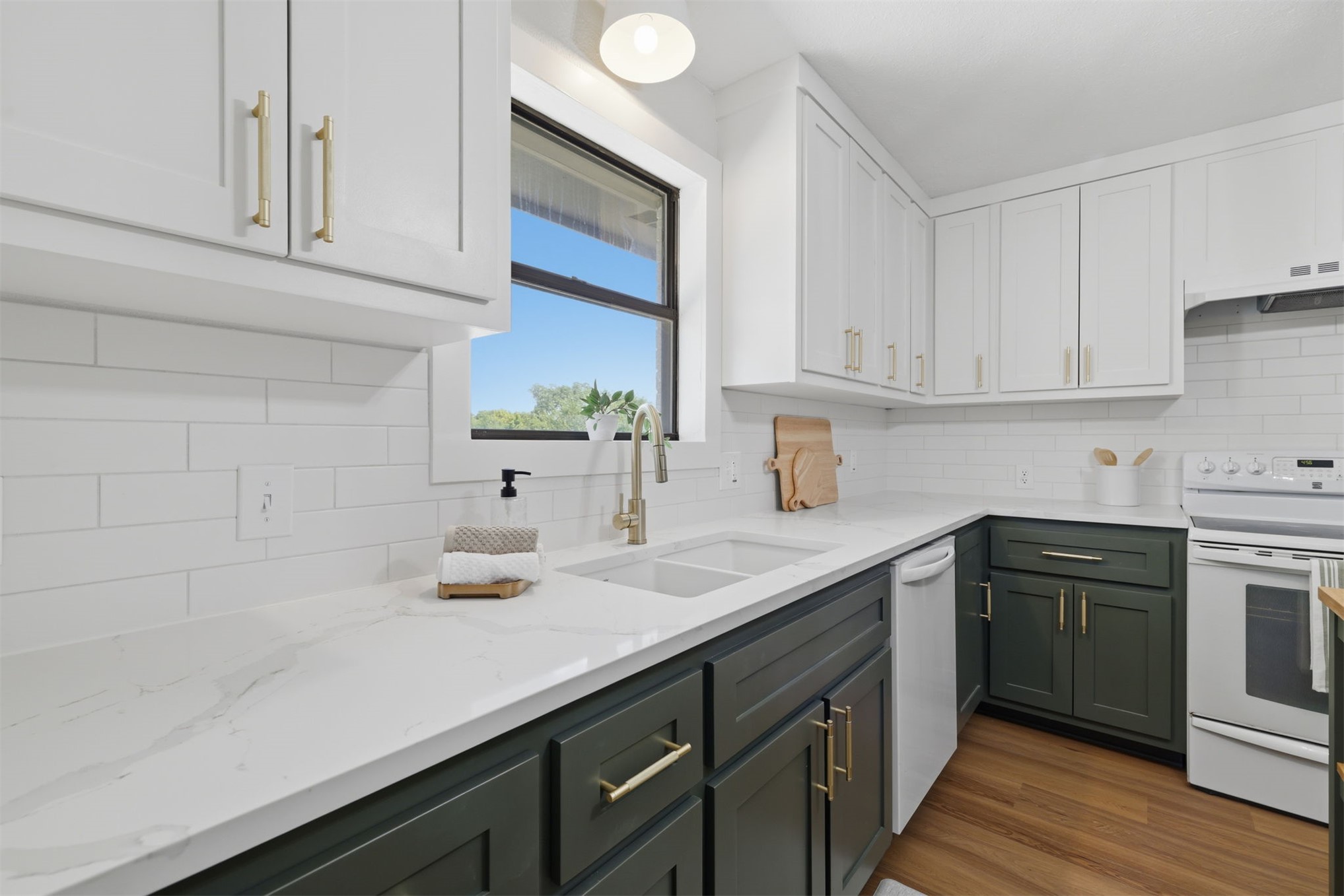 Kitchen featuring two-tone cabinetry with gold-toned hardware, a dual basin sink with a gooseneck faucet, white subway tile backsplash, and wood-finish flooring