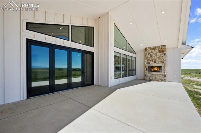 24365 Murphy Road Calhan, CO 80808 - Photo 5 of 48 View of exterior entry featuring a stone fireplace, stone siding, board and batten siding, and a patio