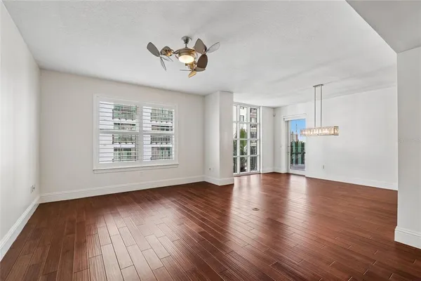 a view of an empty room with wooden floor kitchen view and a window