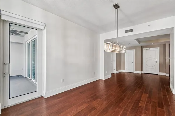 a view of an empty room with wooden floor and kitchen view
