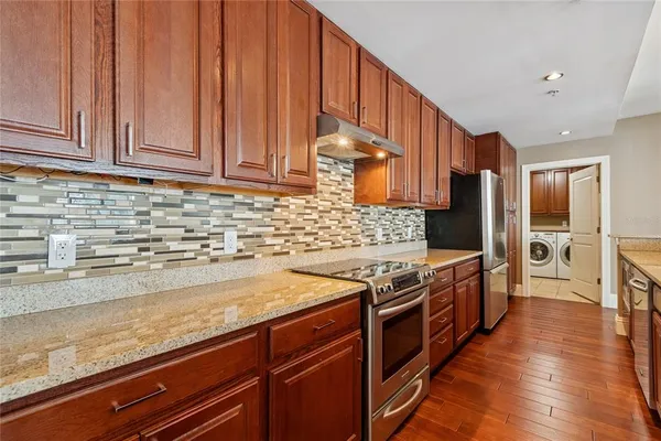 a kitchen with stainless steel appliances granite countertop a refrigerator a sink dishwasher a stove and white countertops with wooden floor