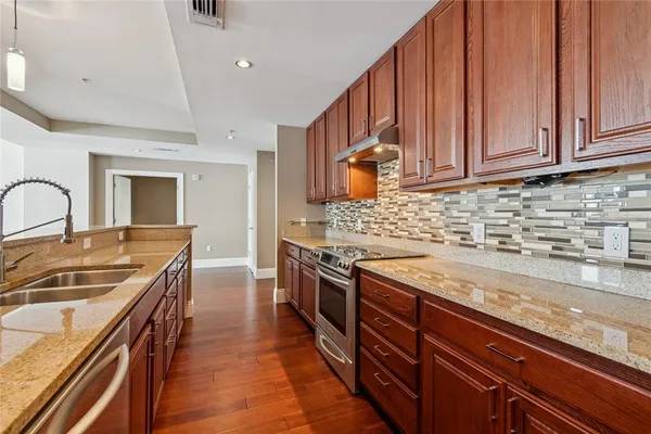 a kitchen with stainless steel appliances granite countertop a refrigerator a stove top oven a sink dishwasher and white cabinets with wooden floor